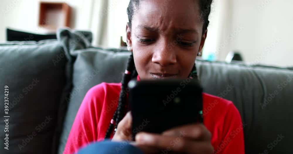 Upset black African teen girl feeling troubled by cellphone news on social media Upset black African teen girl feeling troubled by cellphone news on social media