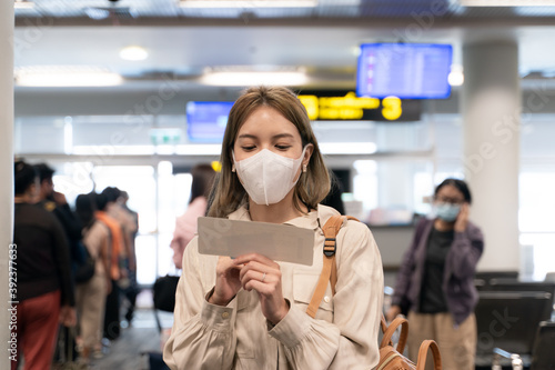 Asian woman wear masks while traveling, holding boarding pass at the airport terminal. New normal, covid19 disease prevention concept.