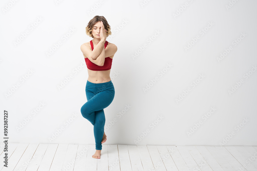 sports woman in a bright room doing yoga in full growth blue leggings and a red tank top sports woman in a bright room doing yoga in full growth blue leggings and a red tank top