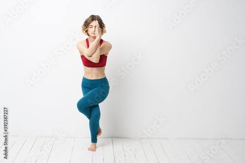 sports woman in a bright room doing yoga in full growth blue leggings and a red tank top