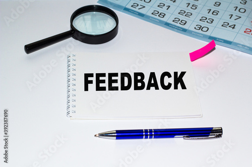 FEEDBACK word written on a notebook. A notebook with a sticker, a calendar, a magnifying glass and a handle on a white background. Sonceptia financial, business, education