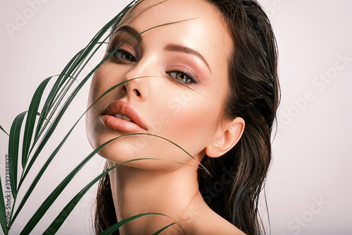 Young beautiful woman with green leaves near face and body. Skin care beauty treatments concept. Closeup girl's face with green leave. White model with clean, health skin of face - posing at studio