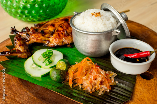 Chicken Inasal served with Garlic Rice, cucumber and Atchara. On a banana leaf on top of wooden platter. It is popular grilled dish from the Western Visayas region of the Philippines photo