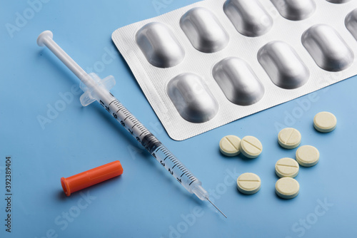 a syringe with a vaccine and pills on a blue background. syringe with antibiotic pills on a blue background.