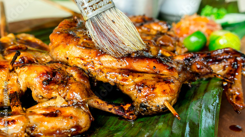 Applying marinade to juicy barbecued chicken with a brush. It is Chicken Inasal, a popular grilled dish in the Philippines. photo