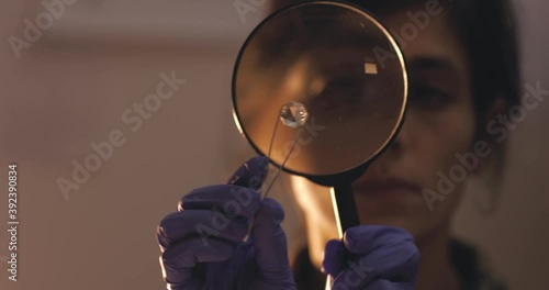 Female holding diamond with tweezer and looking through magnifier.