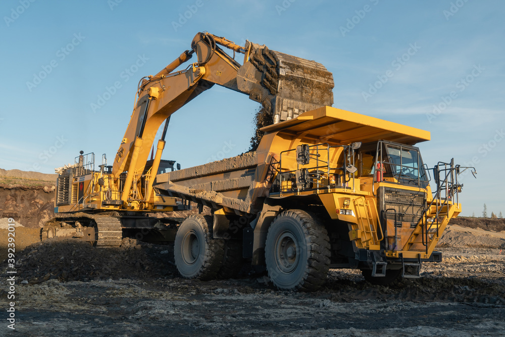 The excavator loads ore into a mining dump truck at the gold mining site. The excavator loads ore into a mining dump truck at the gold mining site.