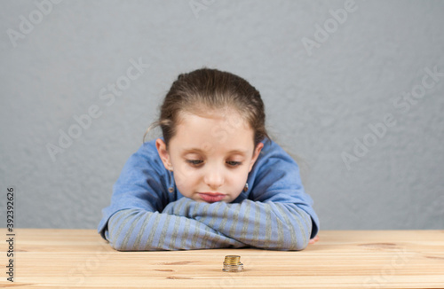 European girl at the table. Stack of coins. Poverty or small income concept.