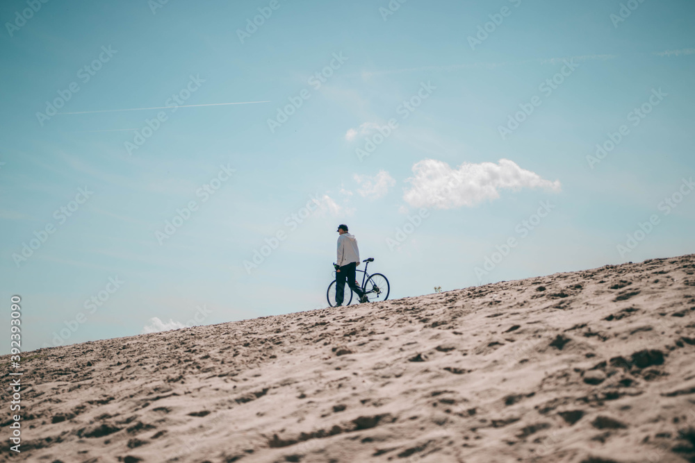 a man with a Bicycle is walking on a mountain of sand