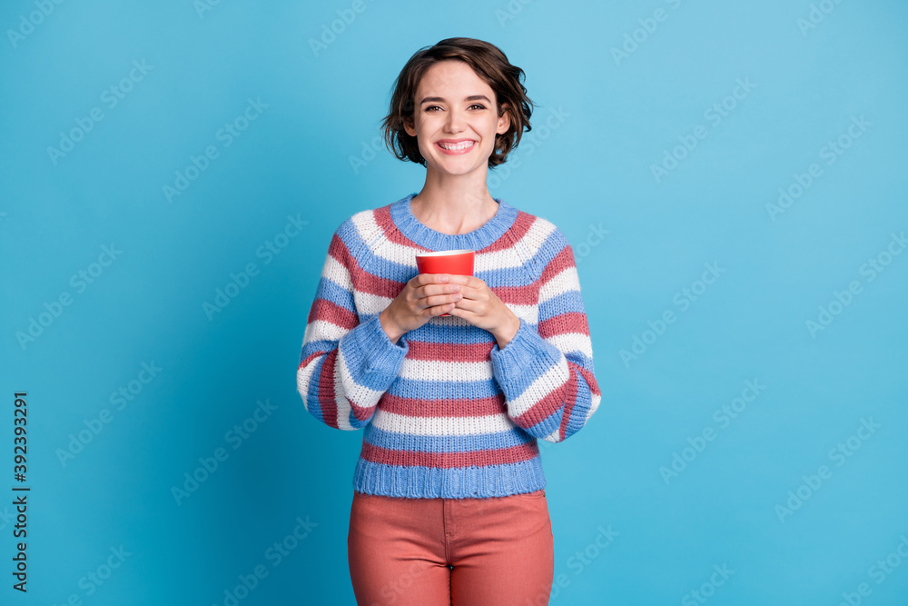 Photo portrait of smiling happy girl keeping red mug wearing striped sweater isolated on vibrant blue color background Photo portrait of smiling happy girl keeping red mug wearing striped sweater isolated on vibrant blue color background