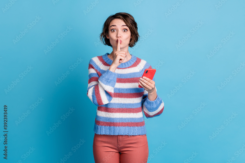 Photo of charming funny unfluencer holding gesturing forefinger near lips asking to stop speaking using smart device isolated over blue color background Photo of charming funny unfluencer holding gesturing forefinger near lips asking to stop speaking using smart device isolated over blue color background