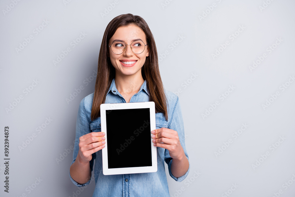 Close up photo of optimistic nice girl show tablet look empty space wear spectacles blue cloth isolated on grey background Close up photo of optimistic nice girl show tablet look empty space wear spectacles blue cloth isolated on grey background