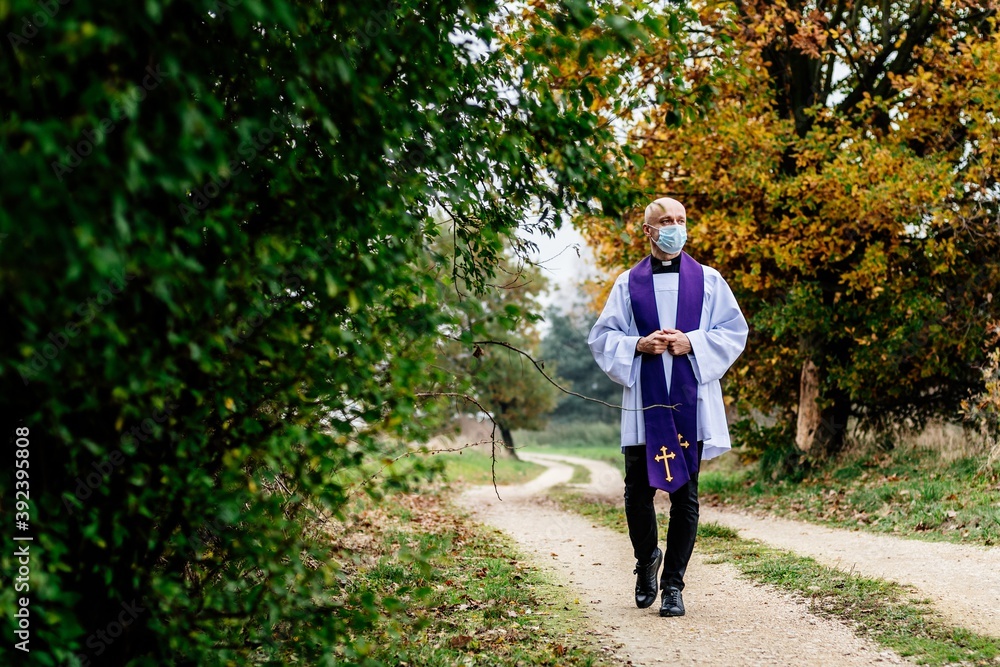 Fototapeta premium Priest in the medical mask is walking through the village.