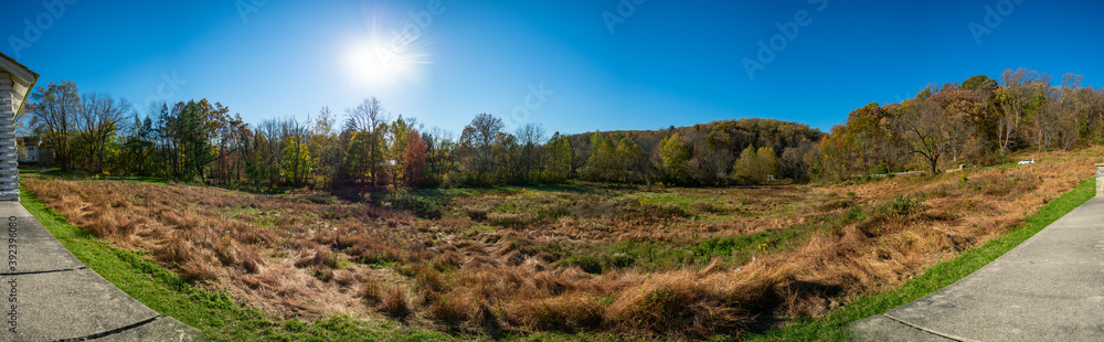 A Panoramic Shot of an Open Field With the Sun Behind Trees at Valley Forge With a Wall at the Bottom of the Frame