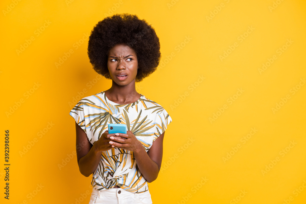 Photo of sad pretty curly hair lady hold telephone look empty space wear print t-shirt isolated over vivid yellow color background Photo of sad pretty curly hair lady hold telephone look empty space wear print t-shirt isolated over vivid yellow color background
