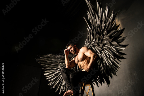 handsome athletic man in black angel costume on black background