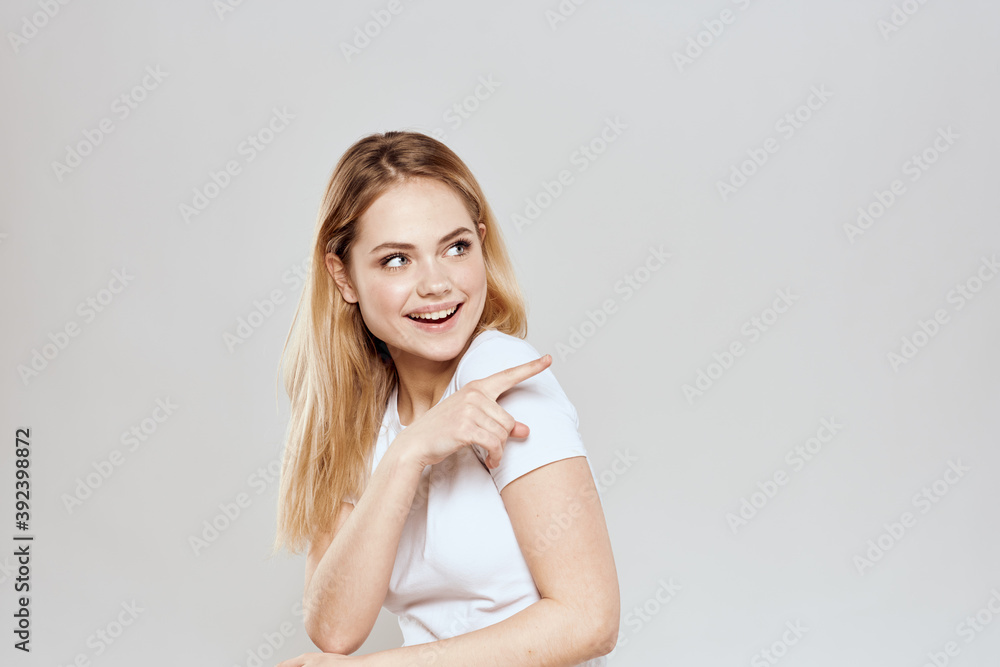cheerful blonde in a white t-shirt gesturing with her hands light background cheerful blonde in a white t-shirt gesturing with her hands light background
