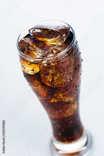 refreshing drink, cold soda with ice cubes in a tall glass on a white background