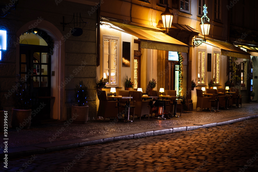 Cafe tables and chairs outside in old cozy street in in Prague. Christmas holidays and travel. Christmas decorations lights.