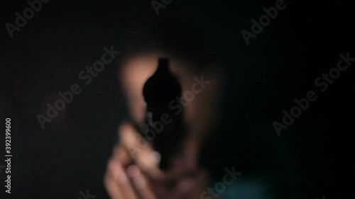 Shot of a man in gree shirt walking and pointing gun towards the camera in dark smoky background.