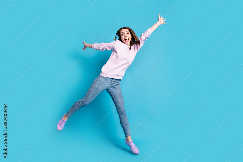 Full length photo of excited careless girl jump enjoy crazy funky weekend raise hands wear lilac pullover isolated over blue color background