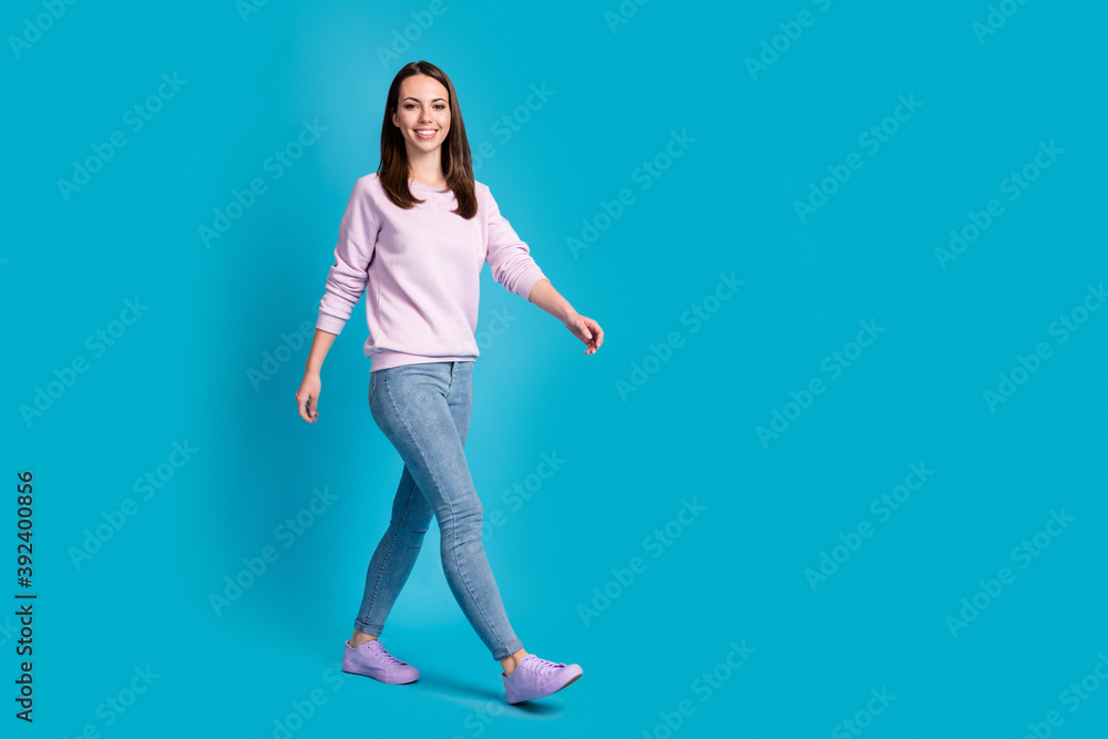 Full length photo of lovely pretty young girl smiling empty space calmly go morning walk park street healthy sporty wear purple sweatshirt jeans denim sneakers isolated blue color background Full length photo of lovely pretty young girl smiling empty space calmly go morning walk park street healthy sporty wear purple sweatshirt jeans denim sneakers isolated blue color background