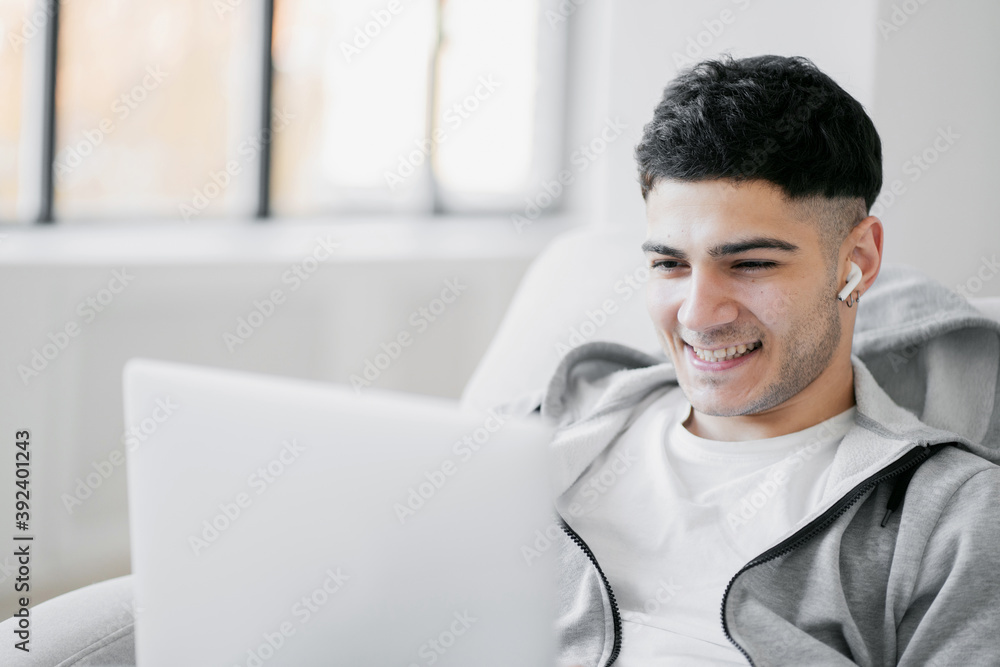 talks to friends via online communication in a social community. Looking at a laptop computer a dark haired man smiles enjoys communicating with loved ones talks to friends via online communication in a social community. Looking at a laptop computer a dark haired man smiles enjoys communicating with loved ones