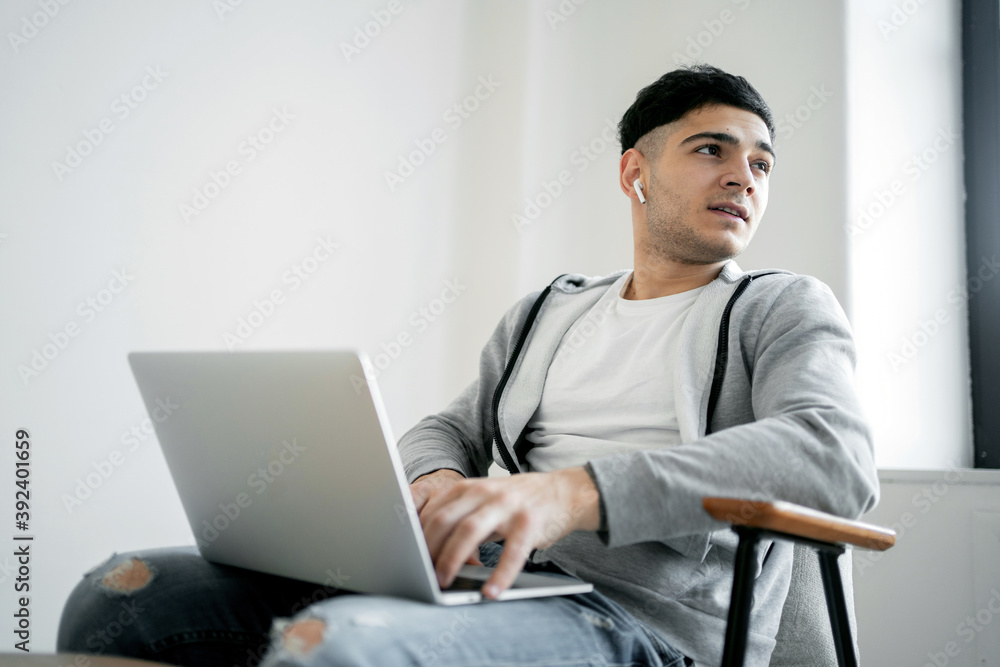young stylish designer dark-haired man works at home on a laptop computer, creates architecture and design projects in his comfortable work chair. young stylish designer dark-haired man works at home on a laptop computer, creates architecture and design projects in his comfortable work chair.