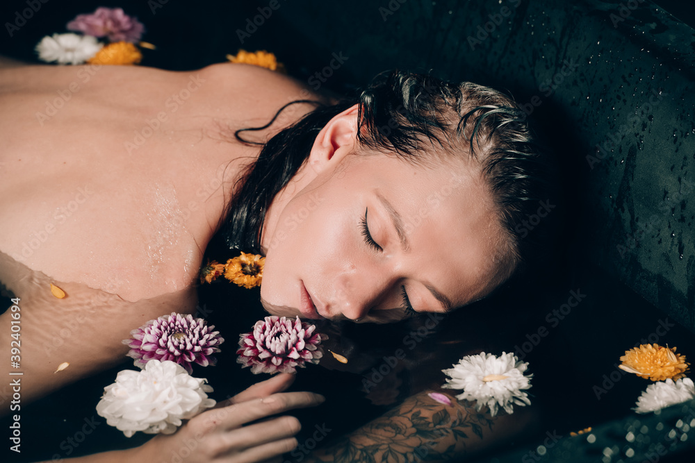 Young pretty brunette woman in bath with water and flowers. Naked model during an unusual photo shoot in a black bath Young pretty brunette woman in bath with water and flowers. Naked model during an unusual photo shoot in a black bath