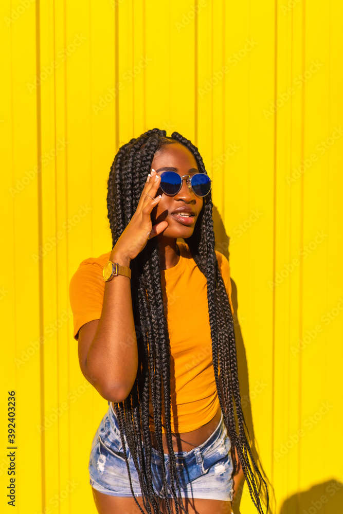 Lifestyle, attractive black girl with long braids, yellow t-shirts and short  jeans on a yellow background. With sunglasses in the urban session in the  city, trap dancer Stock Photo | Adobe Stock