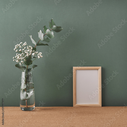 Frame and vase with white flowers and eucalyptus on a dark green background. Mock up  copy space. Folk.
