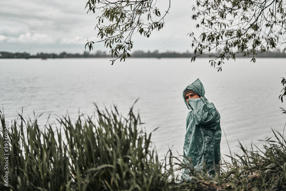 A man in a green raincoat on the shore near the water. Mainly cloudy A man in a green raincoat on the shore near the water. Mainly cloudy