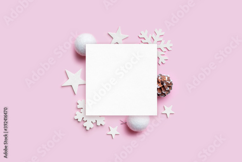 Christmas greeting card mockup with Christmas decorations on pastel pink desk. Blank paper for greeting text. Top view, flat lay