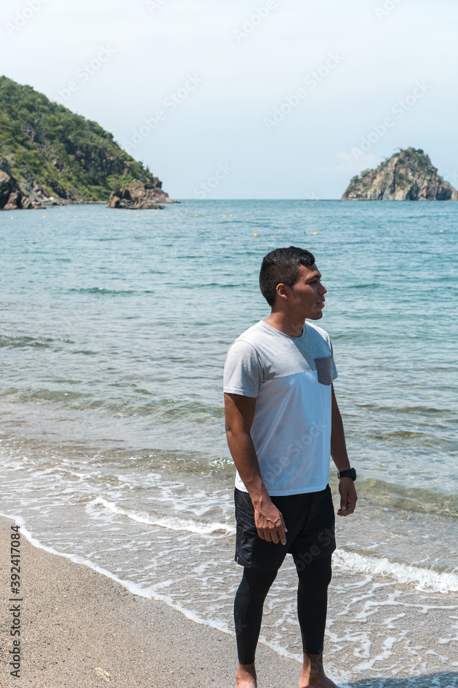 A Hispanic man with a white T-shirt on the beach overlooking the