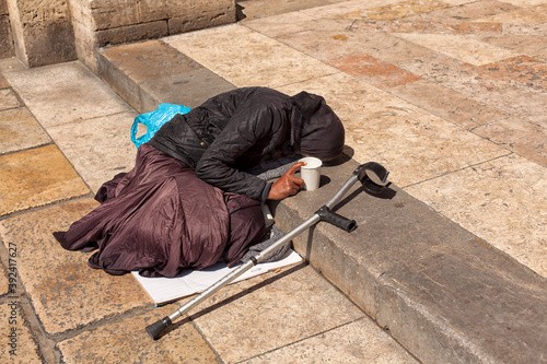 Photo of a beggar woman lying on the ground. a beggar old woman lies on the steps in front of the entrance to the church