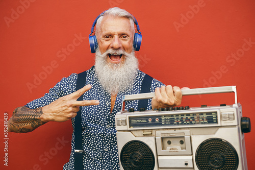 Happy senior man listening to music with wireless headphones and vintage boombox outdoor