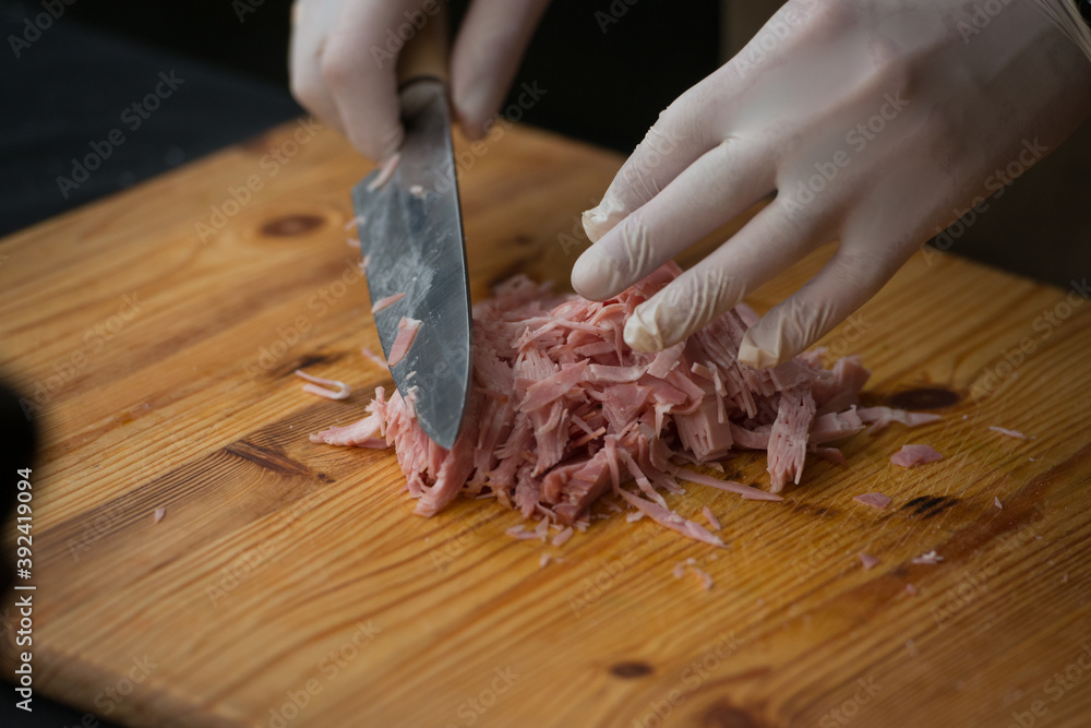 Man in a white gloves chopping bacon with Kitchen knife on a wooden plank