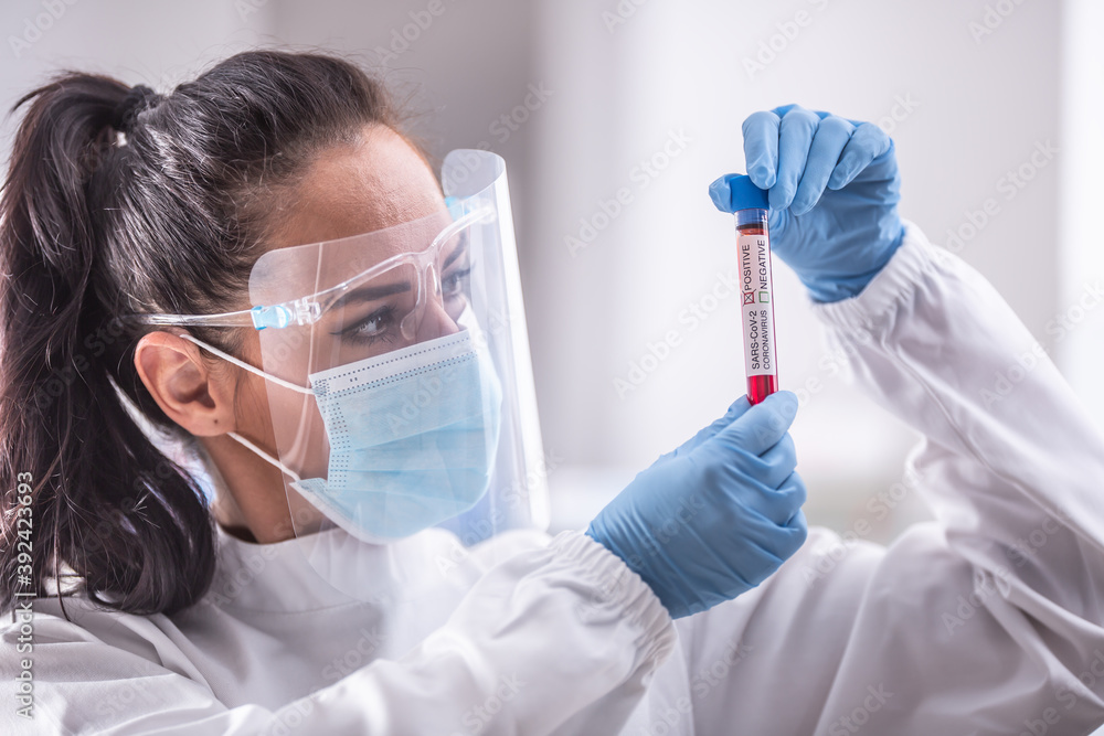 Laboratory worker wearing protective equipment examines an ampule with a Covid-19 test Laboratory worker wearing protective equipment examines an ampule with a Covid-19 test