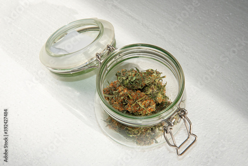 dried buds of marijuana in an open glass jar on a light background