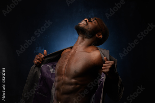 Close up portrait of young african man isolated on black studio background.Photoshoot of real emotions of male model. A man tears his jacket