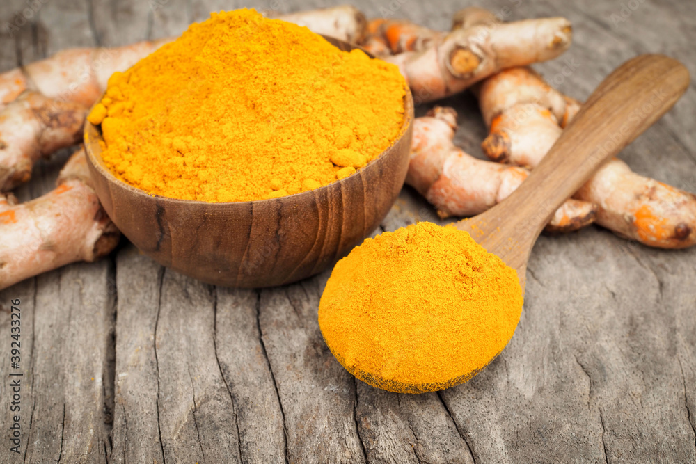 Turmeric powder and fresh turmeric in wooden spoon with green leaf on old wooden table. Herbal Turmeric powder and fresh turmeric in wooden spoon with green leaf on old wooden table. Herbal