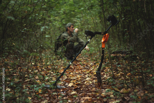 a man works with a metal detector in the forest in camouflage clothes with a backpack behind his back