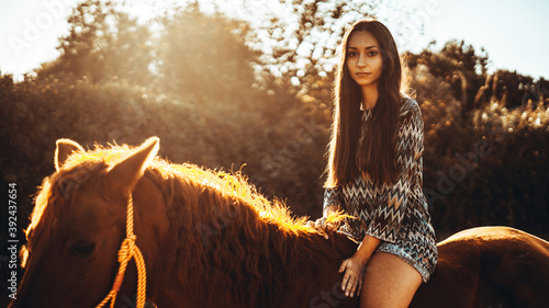 Chica joven andaluza ecuestre montando sobre caballo marron en un campo natural sin silla ni riendas en el sur de españa al atardecer feliz