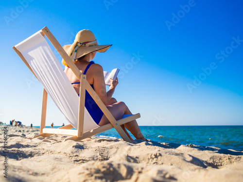 Woman relaxing on beach reading book sitting on sunbed

