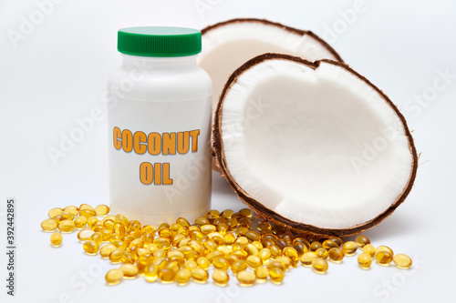 Health care - Nutritional supplement - Bottle of coconut oil with halved coconut on the side and scattered gold gel capsule on the front. Isolated on white background.