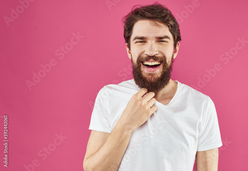 A cheerful guy with a beard laughs on a pink background and gestures with his hands