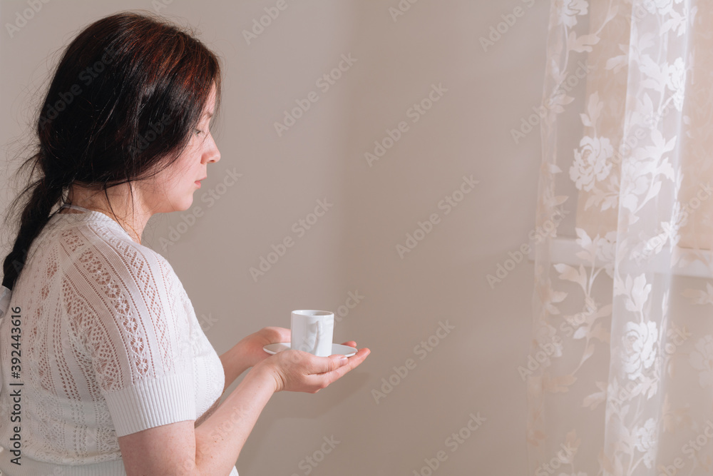 Pretty brunette girl in white clothes holding cup of coffee and enjoying in bed room during morning time at home Pretty brunette girl in white clothes holding cup of coffee and enjoying in bed room during morning time at home