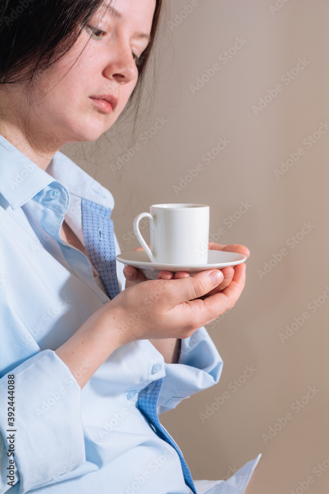 Pretty brunette girl in blue shirt holding cup of coffee and enjoying in bed room during morning time at home Pretty brunette girl in blue shirt holding cup of coffee and enjoying in bed room during morning time at home