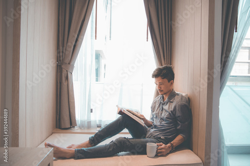 Vintage portrait of a male drinking coffee and reading in a room by the window.