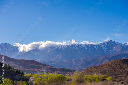 Daytime wide angle shot of Beautiful landscape of snow capped mountains and bushes and a village in the valley. Atlas, Morocco. © dhvstockphoto